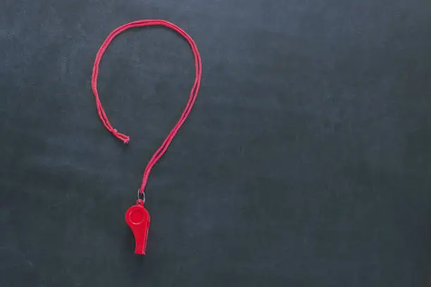 Photo of Sports whistle on a red lace. It is laid out in the form of a question mark. Concept- sport competition, referee, statistics, challenge, friendly match.