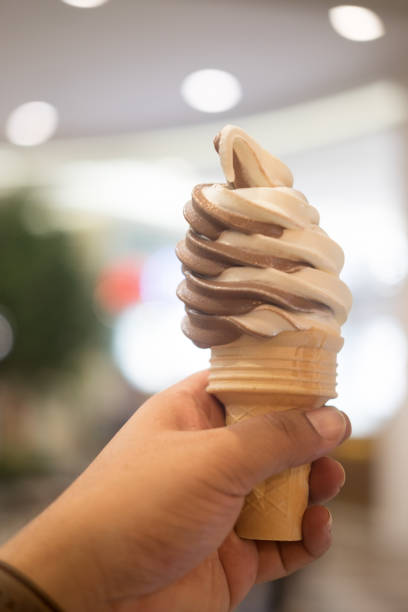 istock Vanilla and chocolate soft ice cream waffled cone in young hand 1005456400