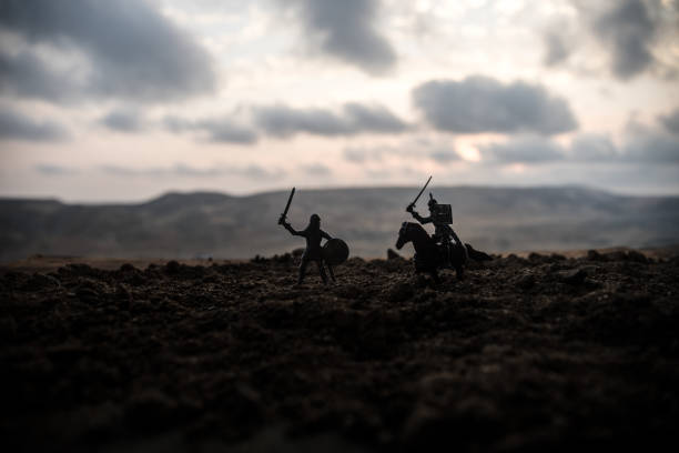 istock Medieval battle scene with cavalry and infantry. Silhouettes of figures as separate objects, fight between warriors on sunset foggy background. 1005463454
