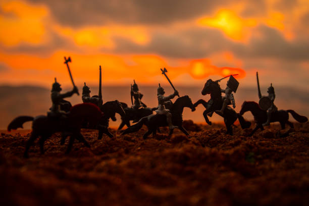 istock Medieval battle scene with cavalry and infantry. Silhouettes of figures as separate objects, fight between warriors on sunset foggy background. 1005463456