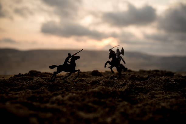 istock Medieval battle scene with cavalry and infantry. Silhouettes of figures as separate objects, fight between warriors on sunset foggy background. 1005463462