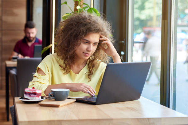 istock Curly student studying, working with laptop sitting in cafe. 1005473500