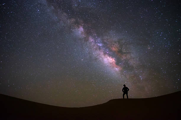 istock Milky way galaxy with a man standing and watching at Tar desert, Jaisalmer, India. 1005473836