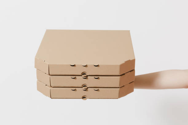 istock Close up female holds in hand stack pizza in clear empty blank cardboard brown flatboxes, food order pizza boxes isolated on white background. Delivery service concept. Copy space. Advertising area. 1005490086