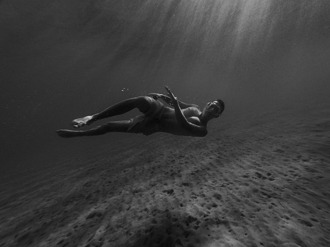 Black and white photo of a free diver drifting near the sea bottom