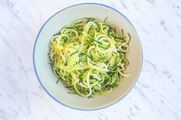 Zucchini spaghetti or noodles (zoodles) in a bowl with marble background Top view overhead.