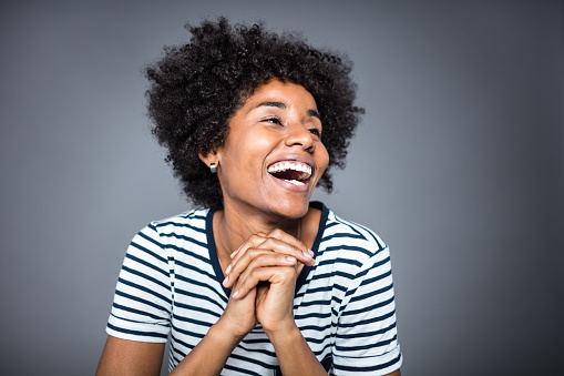 Close-up of happy young woman looking away against gray background. Cheerful female is with afro hairstyle. She is in striped t-shirt.