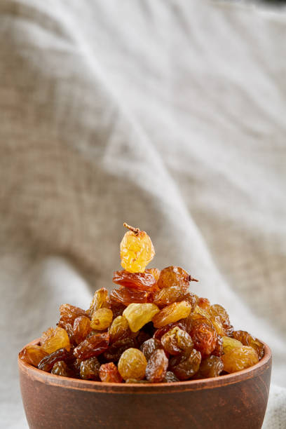 Close-up picture of ceramic clay bowl with golden raisins on light grey tablecloth or napkin, copy space, selective focus. Yummy and gourmet snack. Healthy lifestyle concept.