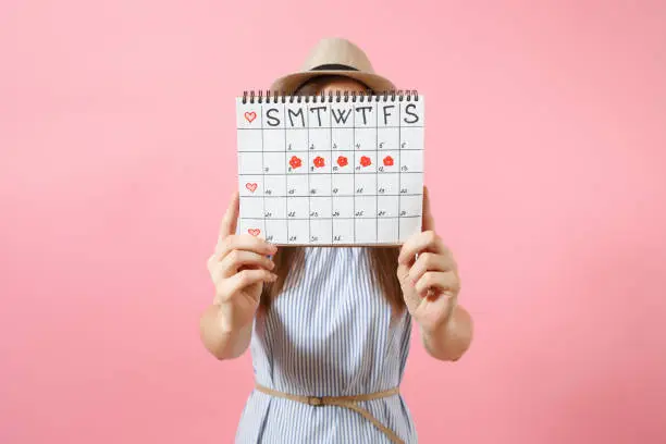 Photo of Portrait of woman in blue dress cover face, hiding behind periods calendar for checking menstruation days isolated on trending pink background. Medical, healthcare, gynecological concept. Copy space.