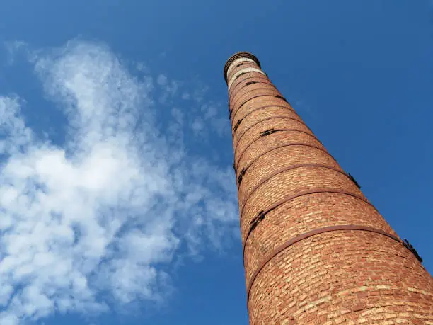 Photo of Red brick pipe on the background of the blue sky with white clouds, bottom view