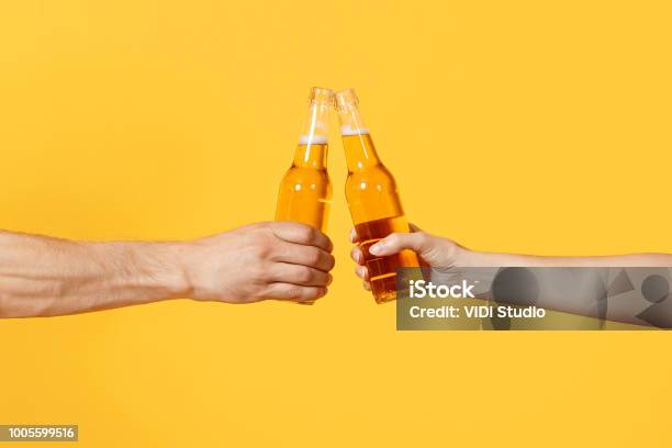 Close Up Cropped Of Woman And Man Two Hands Horizontal Holding Lager Beer Glass Bottles And Clinking Isolated On Yellow Background Sport Fans Cheer Up Friends Leisure Lifestyle Concept Copy Space Stock Photo - Download Image Now