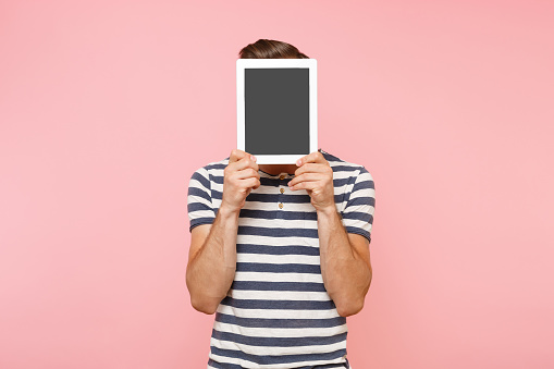 Portrait of young man holding tablet computer with blank black empty screen display touchscreen copy space isolated on trending pastel pink background. Technology lifestyle concept. Advertising area