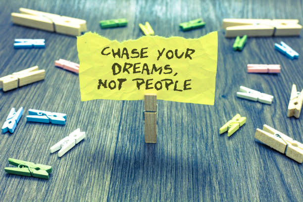 istock Handwriting text Chase Your Dreams, Not People. Concept meaning Do not follow others chasing goals objectives Paperclip hold written torn page many clips laid on bluish wooden floor. 1005608080