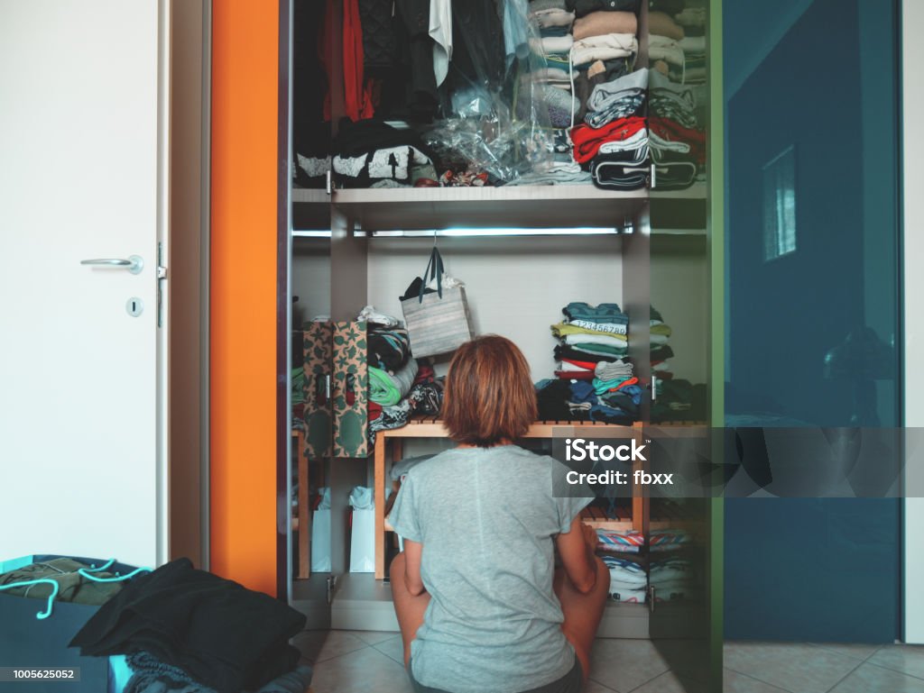 Woman looking at wardrobe, home interior, desperate housewife, cleaning home, rear view sitting, toned vintage style. Closet Stock Photo