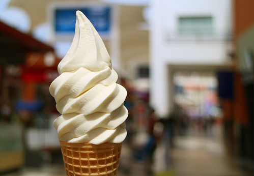Front view of vanilla milk soft serve ice cream cone in the sunlight, with blurred city center view in background