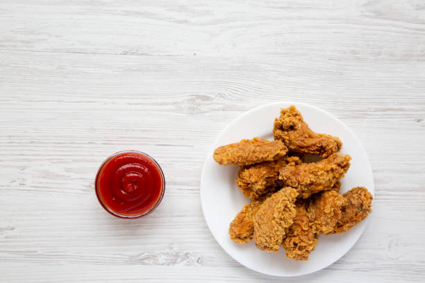 istock Chicken wings on a round white plate with ketchup on a white wooden table, top view. Flat lay, overhead, from above. Copy space. 1005659156