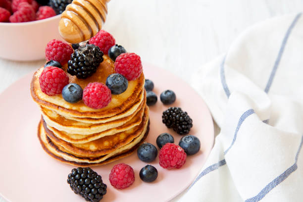 Tasty pancakes with berries and honey on a pink plate, side view. Closeup.