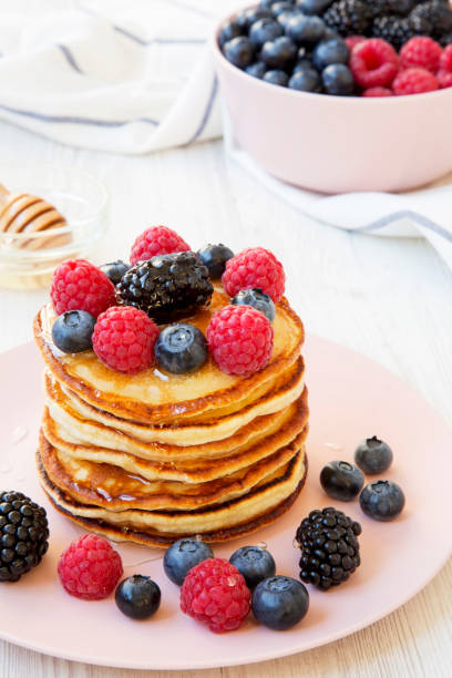 Pancakes with berries and honey on a pink plate, side view. Closeup.