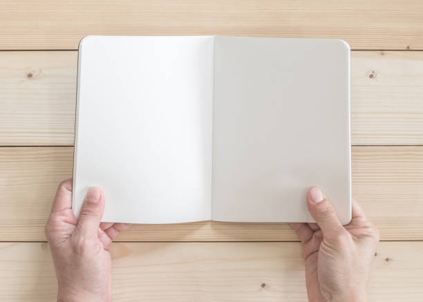 istock Blank open pocket book mock up, catalog magazines, or note template with paper texture copyspace in person's hands on white pine wood table 1005715538