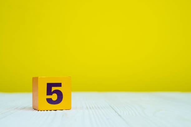 istock Square block puzzle number 5 on table with yellow background 1005717960