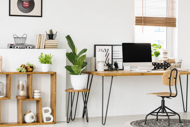 istock Plant on stool next to wooden desk with computer desktop in white workspace interior. Real photo 1005736428