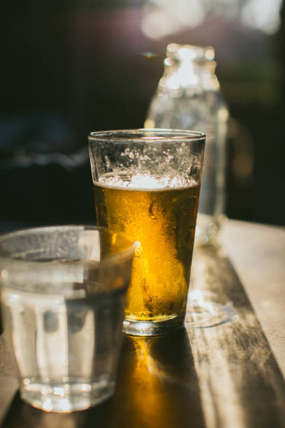 istock Beer Shining in Light next to Water Glass 1005741236