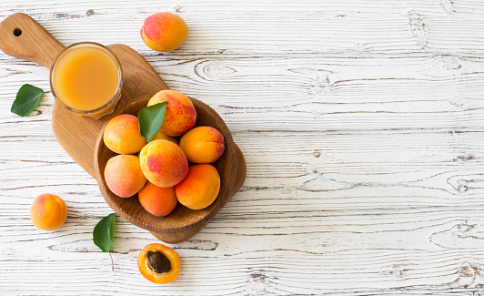 Ripe apricots and glass of juice  in wooden bowl on white wood background. Flat lay. Copy space