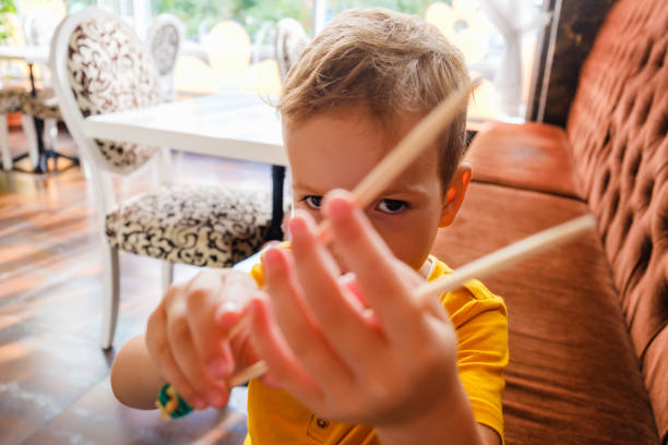 istock Little funny boy eats Japanese traditional rolls with chopsticks, eating sushi 1005798290