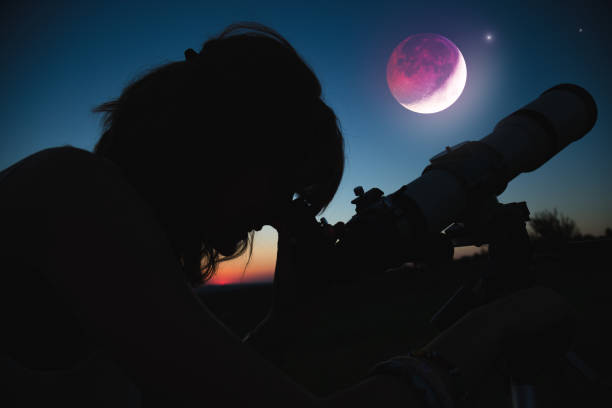 istock Girl looking at lunar eclipse through a telescope. My astronomy work. 1005803400