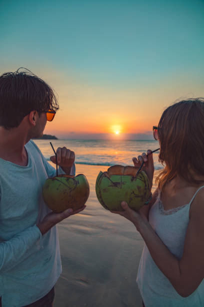 istock Couple drinking cocnut juice while watching the sunset over the ocean in Bali, Indonesia. 1005806074