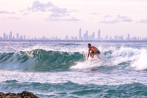This is Australia - age is just a number mature man riding a malibu surfboard on a small wave at sunset with city on the horizon active lifestyle when retired