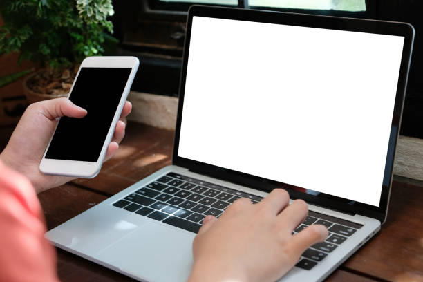 istock Man hands typing laptop computer and smart phone with blank screen for mock up template background, business technology and lifestyle background concept 1005815130
