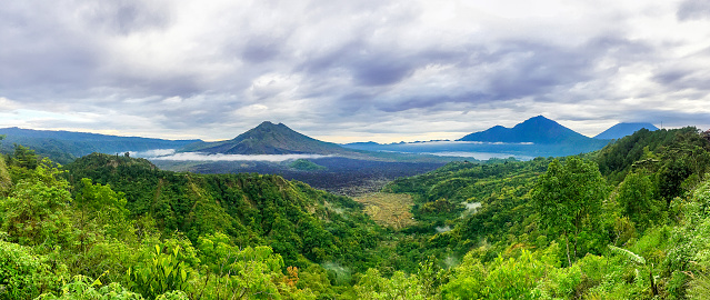 A serene landscape of lush green hills dotted with quaint farmhouses and distant mountains, all illuminated by the warm glow of the setting sun