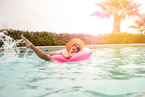 A stock photo of a young woman enjoying the summer weather in a swimming pool with a large inflatable ring.
