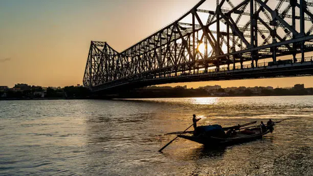 Silhouette of Howrah Bridge at the time of Sunrise.  Howrah Bridge is a bridge with a suspended span over the Hooghly River in West Bengal.