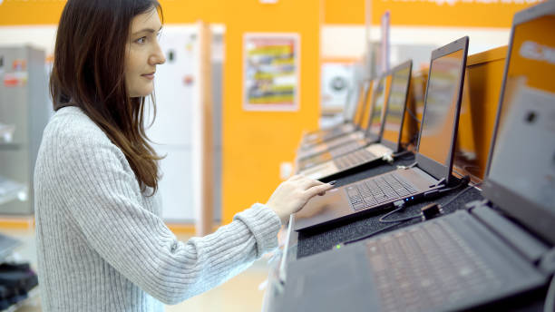istock Young brunette woman chooses a laptop in a hardware store 1005857600