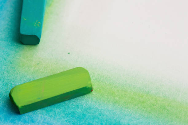 Pastel crayons in green and blue draw a smudgy border on a white sketchpad, leaving copy space.