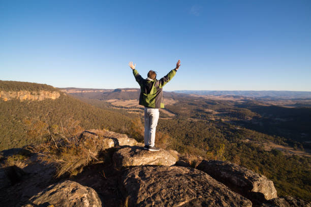 istock Male bushwalker standing on rock pinnacle arms outstretched 1005863912