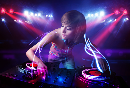 Pretty young disc jockey girl playing music with light beam effects on stage