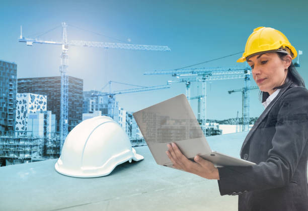 istock Woman engineer holding laptop with helmet on construction building with cranes 1005871286
