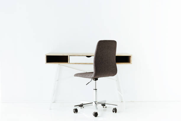 istock stylish empty work table and wheeled chair in front of white wall 1005882702