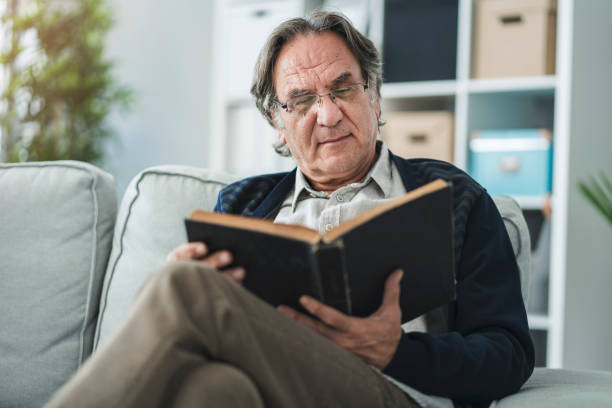 istock Old man reading book at home 1005889120