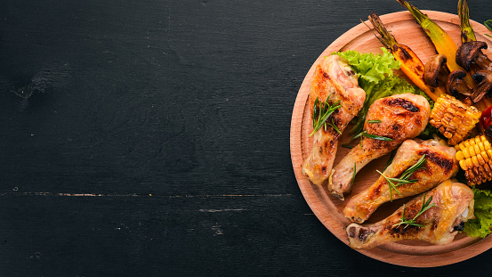 Baked chicken legs with spices and vegetables. On a wooden background. Top view. Copy space.