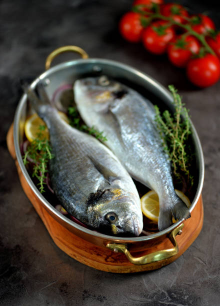 istock Two fresh raw dorado fish with lemon, red onion and thyme in a copper frying pan. 1005890502