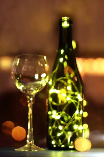 blurred  silhouettes of bottle and glass in the lights of garlands on table