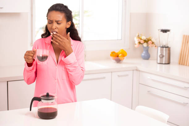 donna sbadigliante con una tazza di caffè in cucina a casa al mattino. - yawning women drink coffee cup foto e immagini stock