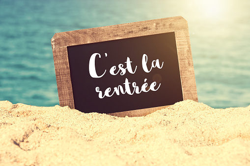 C'est la rentrée (meaning Back to school in French) written on a vintage chalkboard in the sand of a beach