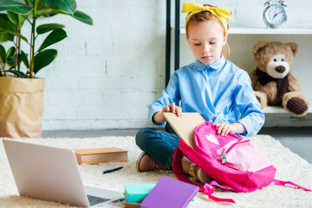istock cute little child packing school bag while sitting on carpet at home 1005934348