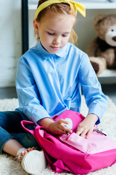 istock adorable child packing pink school bag at home 1005934438