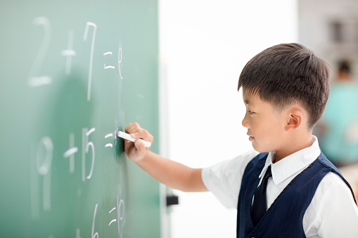 Happy schoolboy writing answer on  blackboard